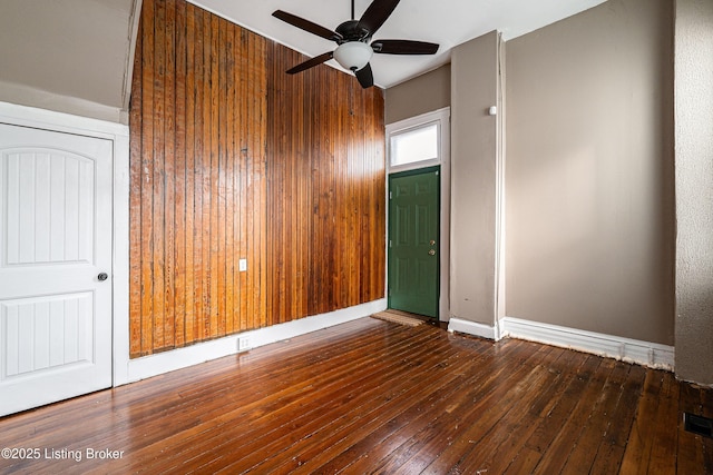 empty room featuring ceiling fan, dark hardwood / wood-style floors, and wooden walls