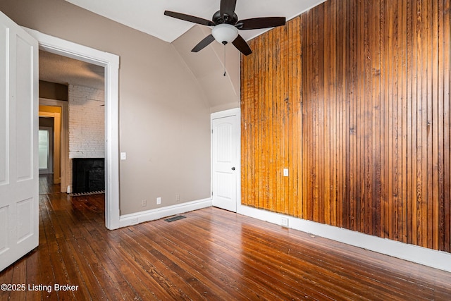 empty room featuring ceiling fan, dark wood-type flooring, lofted ceiling, and a large fireplace