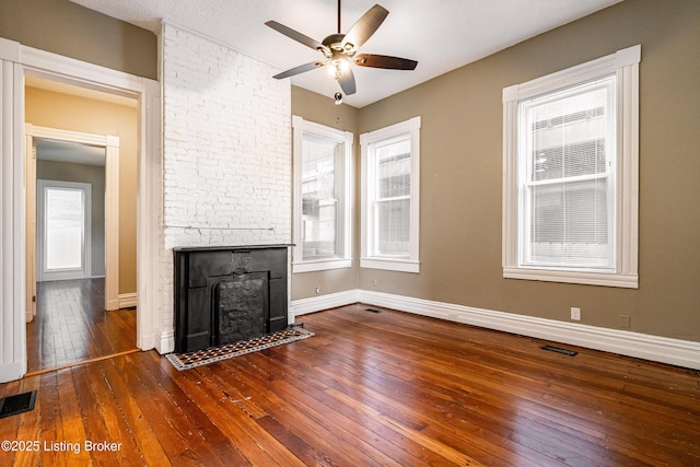 unfurnished living room featuring ceiling fan, dark wood-type flooring, a stone fireplace, and a healthy amount of sunlight