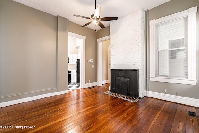 unfurnished living room with ceiling fan, wood-type flooring, a stone fireplace, and a healthy amount of sunlight