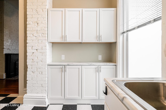 kitchen with white cabinets, brick wall, and a brick fireplace