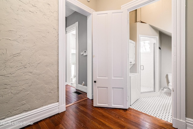 corridor with stacked washer / dryer and dark hardwood / wood-style flooring