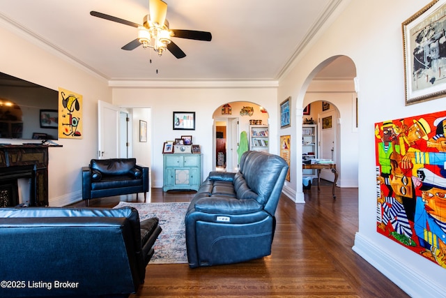 living room with ornamental molding, dark wood-type flooring, and ceiling fan