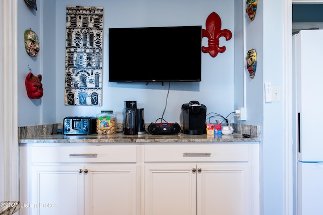 bar with white cabinetry, light stone countertops, and white fridge