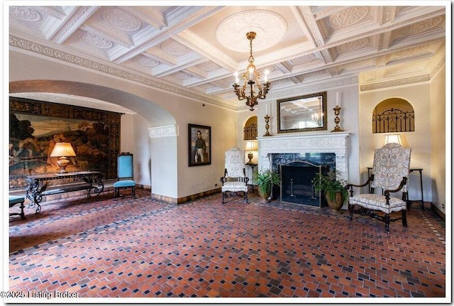 carpeted living room featuring coffered ceiling, a notable chandelier, a high end fireplace, and ornamental molding