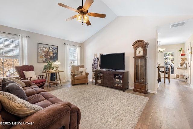 living room featuring ceiling fan with notable chandelier, vaulted ceiling, and light hardwood / wood-style floors