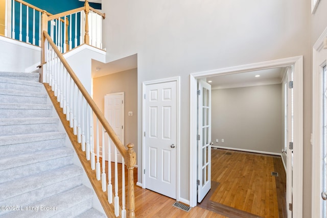 stairs with hardwood / wood-style flooring, ornamental molding, and a towering ceiling