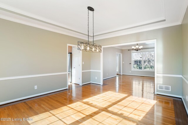 unfurnished dining area with a raised ceiling, ornamental molding, and hardwood / wood-style floors