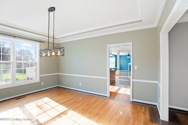 unfurnished dining area with a raised ceiling, crown molding, and hardwood / wood-style floors