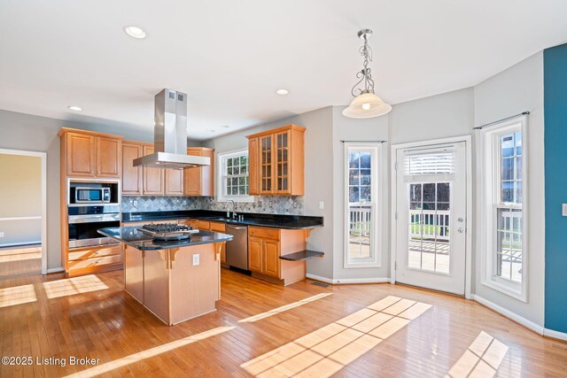 kitchen featuring appliances with stainless steel finishes, a center island, decorative backsplash, island range hood, and a breakfast bar