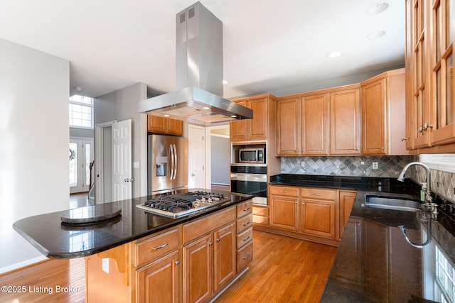 kitchen with appliances with stainless steel finishes, a center island, light hardwood / wood-style floors, sink, and island range hood