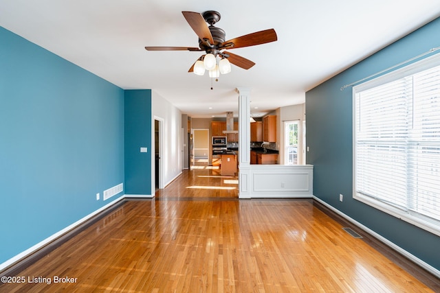 unfurnished living room with light hardwood / wood-style floors, ceiling fan, and ornate columns