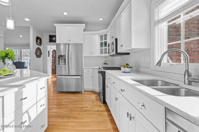 kitchen featuring sink, white cabinetry, decorative light fixtures, light hardwood / wood-style flooring, and appliances with stainless steel finishes