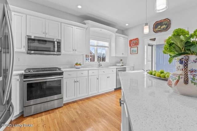 kitchen featuring appliances with stainless steel finishes, pendant lighting, sink, white cabinets, and light wood-type flooring