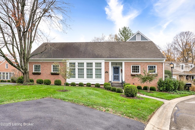 view of front of property with a front lawn, brick siding, and a shingled roof