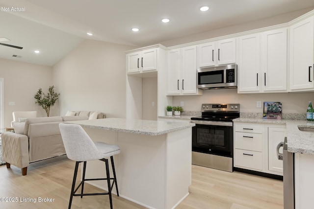 kitchen featuring stainless steel appliances, a center island, white cabinets, and light stone counters