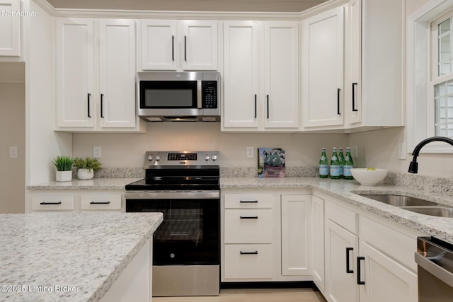 kitchen with white cabinets, light stone counters, stainless steel appliances, and a sink