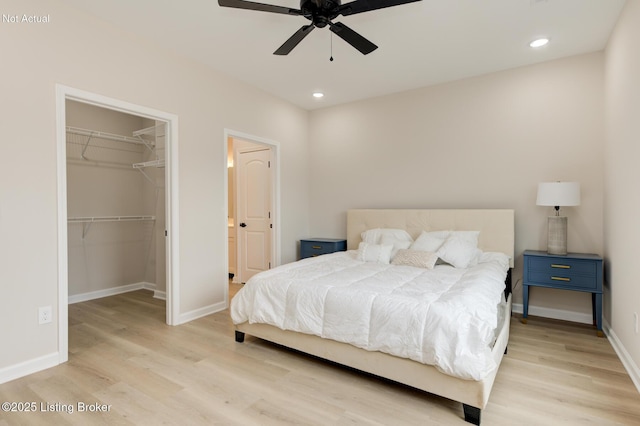 bedroom with a walk in closet, light wood-style flooring, and baseboards