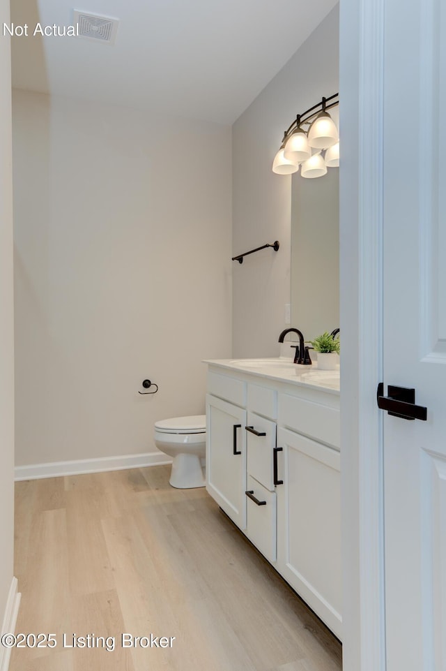 half bathroom with toilet, wood finished floors, visible vents, vanity, and baseboards