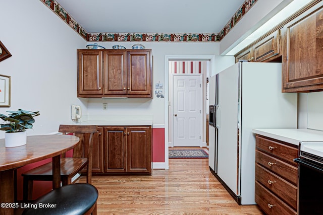 kitchen with white refrigerator with ice dispenser, range, and light hardwood / wood-style floors