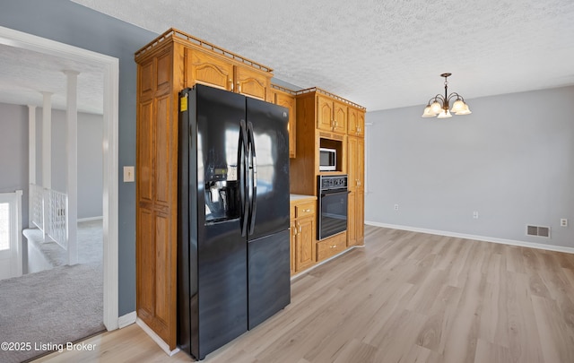 kitchen with a chandelier, a textured ceiling, hanging light fixtures, light hardwood / wood-style floors, and black appliances