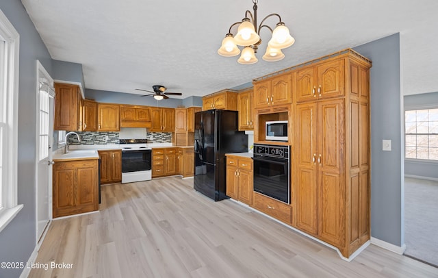 kitchen featuring pendant lighting, sink, backsplash, black appliances, and light wood-type flooring