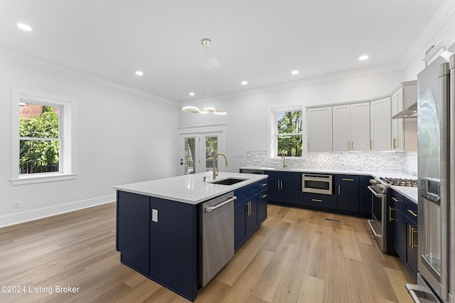 kitchen featuring sink, hanging light fixtures, stainless steel appliances, an island with sink, and white cabinets