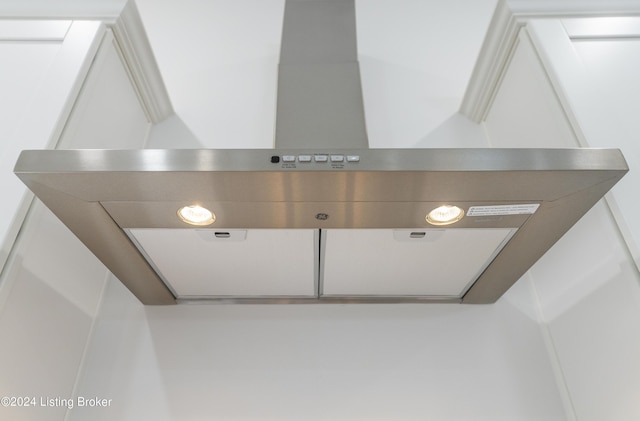 room details featuring wall chimney range hood, exhaust hood, and white cabinets