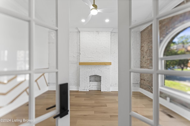 living room with a healthy amount of sunlight, wood-type flooring, brick wall, and a brick fireplace