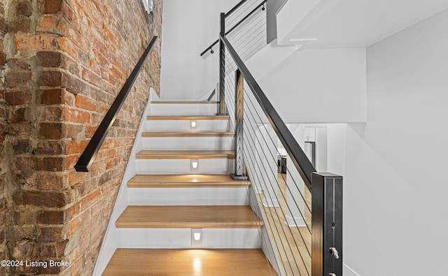 staircase with hardwood / wood-style floors and brick wall