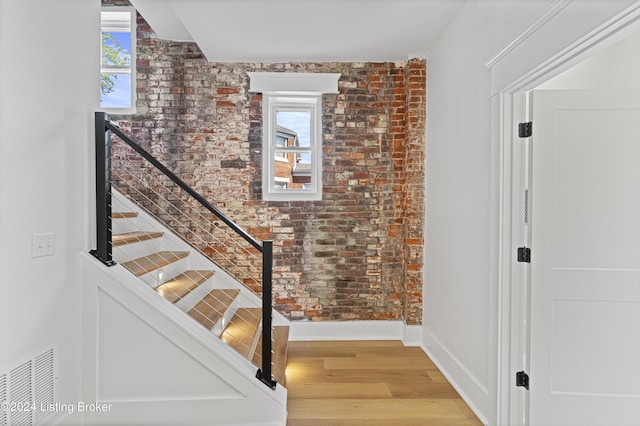 staircase featuring hardwood / wood-style flooring, a healthy amount of sunlight, and brick wall