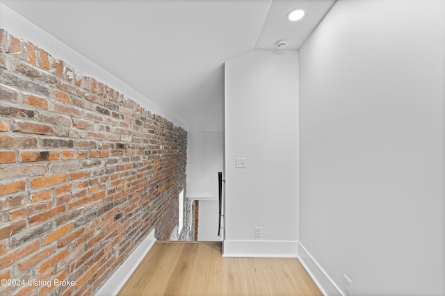 corridor with brick wall, lofted ceiling, and hardwood / wood-style floors