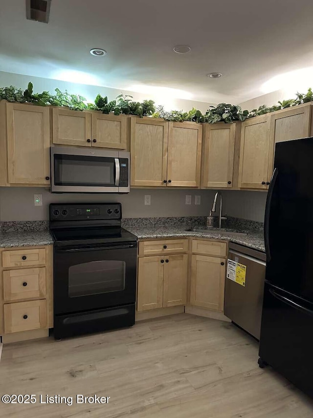 kitchen with sink, light hardwood / wood-style flooring, light stone counters, black appliances, and light brown cabinetry