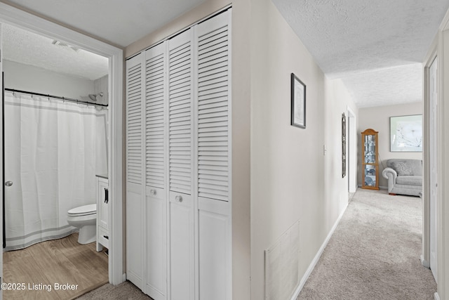 corridor with light carpet and a textured ceiling