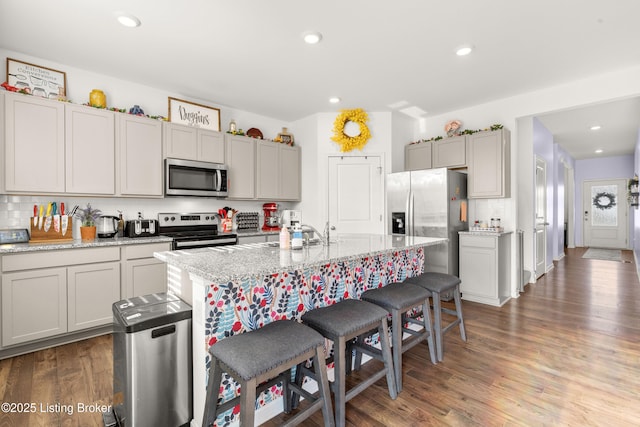 kitchen featuring a kitchen island with sink, light stone countertops, stainless steel appliances, and dark hardwood / wood-style floors