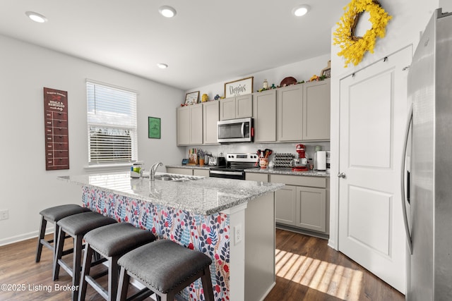 kitchen with gray cabinets, a breakfast bar, an island with sink, light stone counters, and stainless steel appliances