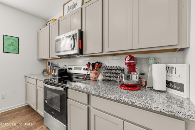 kitchen with stainless steel appliances, light stone countertops, dark hardwood / wood-style floors, and decorative backsplash