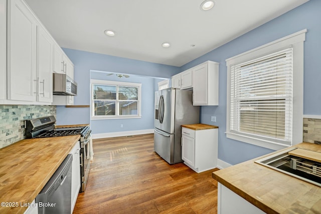 kitchen with hardwood / wood-style flooring, appliances with stainless steel finishes, white cabinetry, backsplash, and wood counters