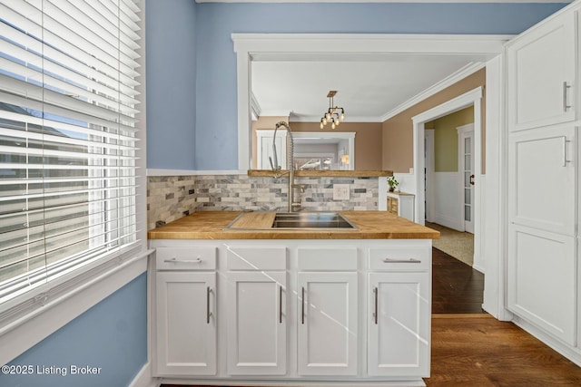 kitchen with dark wood-type flooring, butcher block countertops, sink, ornamental molding, and white cabinets