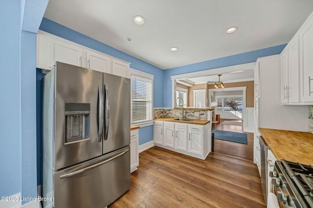 kitchen featuring appliances with stainless steel finishes, butcher block countertops, white cabinets, decorative backsplash, and light hardwood / wood-style flooring