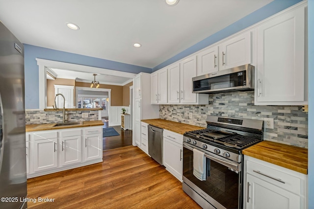 kitchen with butcher block countertops, stainless steel appliances, light hardwood / wood-style floors, white cabinets, and decorative backsplash