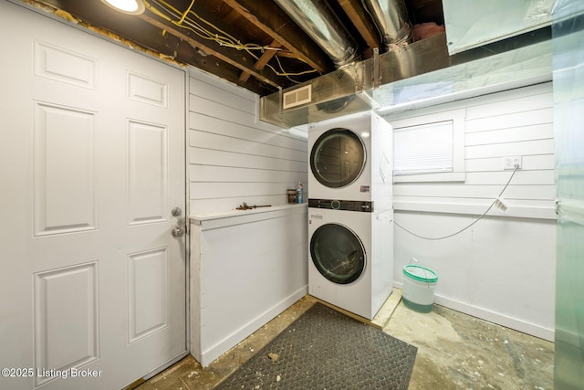 laundry area featuring stacked washer / drying machine and wooden walls