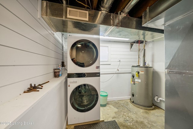 laundry area with water heater, stacked washer and dryer, heating unit, and wood walls