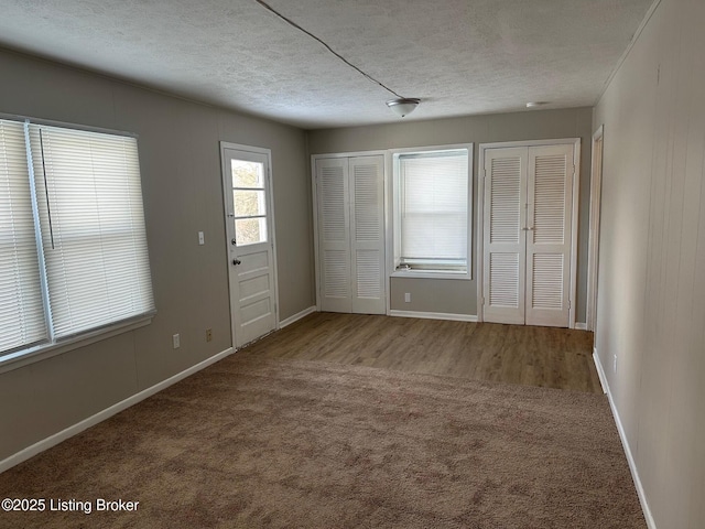 unfurnished bedroom with carpet floors, a textured ceiling, and two closets