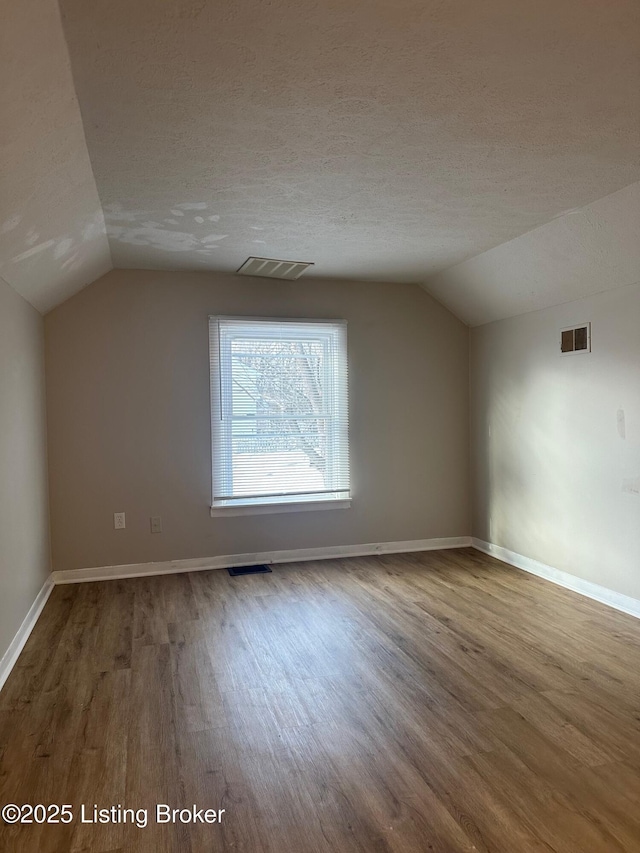 additional living space featuring wood-type flooring, vaulted ceiling, and a textured ceiling