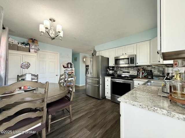 kitchen featuring backsplash, stainless steel appliances, white cabinets, decorative light fixtures, and a chandelier