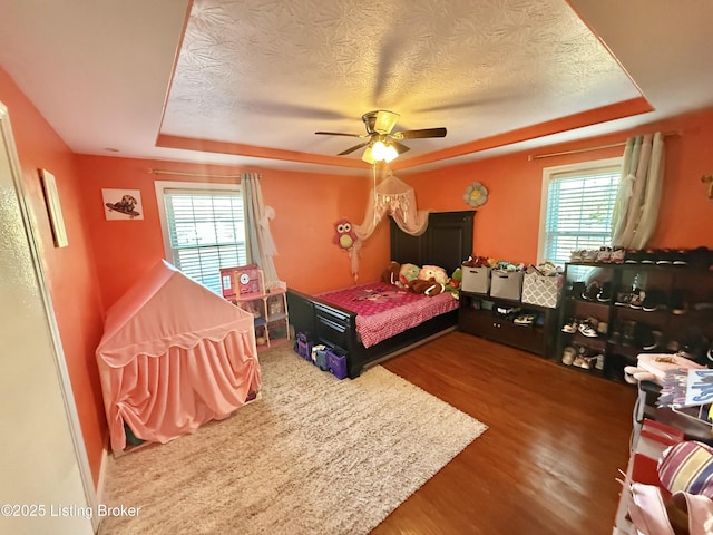 bedroom featuring multiple windows, wood-type flooring, a raised ceiling, and ceiling fan