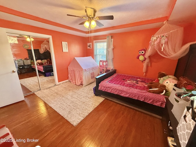 bedroom featuring hardwood / wood-style flooring, ceiling fan, a raised ceiling, and a closet