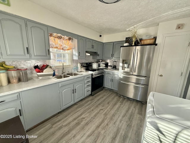 kitchen with sink, a textured ceiling, light wood-type flooring, appliances with stainless steel finishes, and gray cabinets