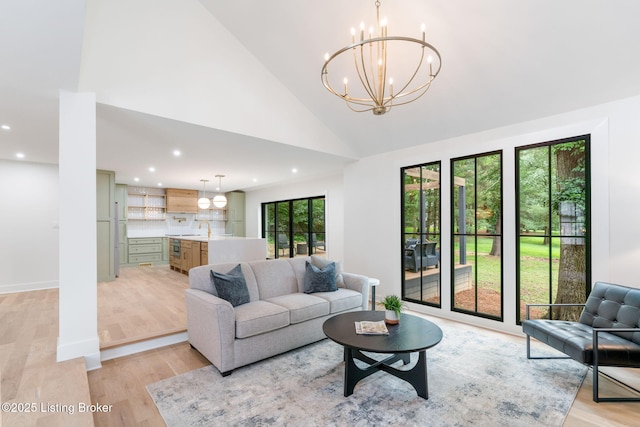 living room with a notable chandelier, sink, high vaulted ceiling, and light wood-type flooring